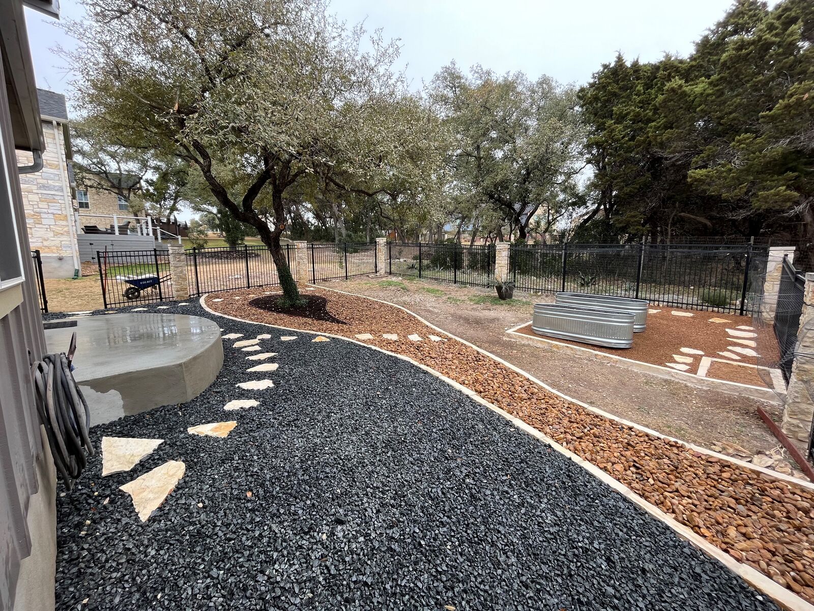 A Pioneer backyard build: fire pit, gravel and stone pathways, and planted beds behind a home